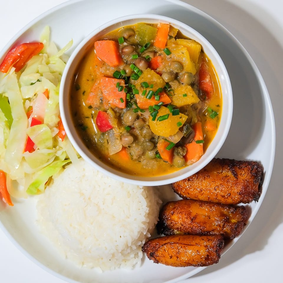 Plate of white rice, vegetable and bean stew, sautéed cabbage, and fried plantains.